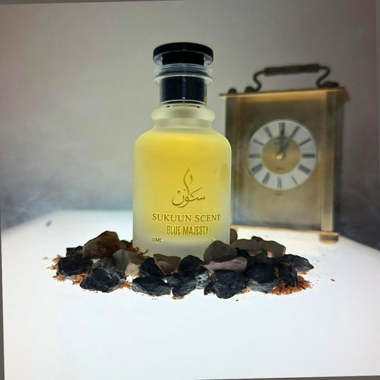 Sukuun Scent Blue Majesty Eau de Parfum 50ML frosted glass bottle with black cap, surrounded by dark stones and wood shavings.