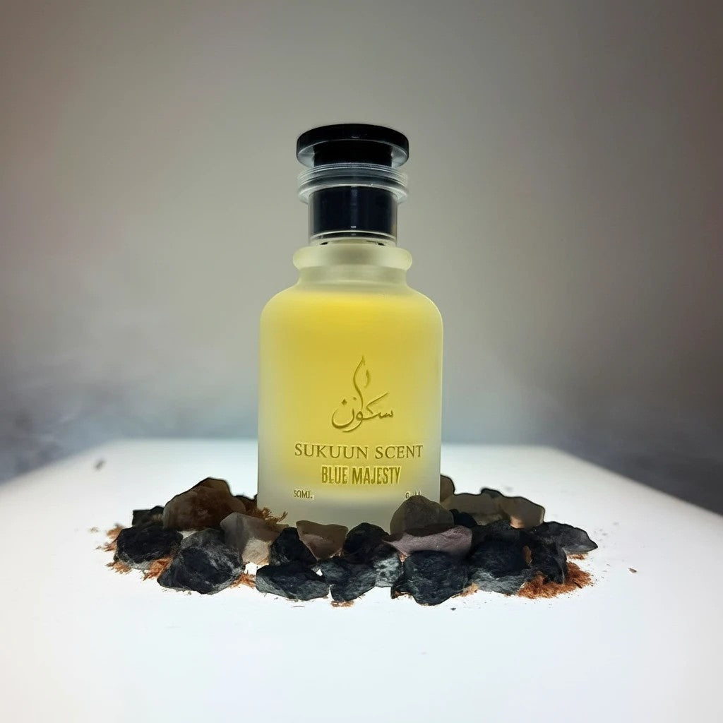 Sukuun Scent Blue Majesty Eau de Parfum 50ML frosted glass bottle with yellow liquid, surrounded by dark stones.
