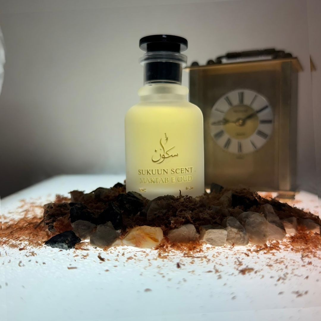 Sukuun Scent Maktab E Oud Eau de Parfum 50ML bottle surrounded by oud chips and a vintage clock.