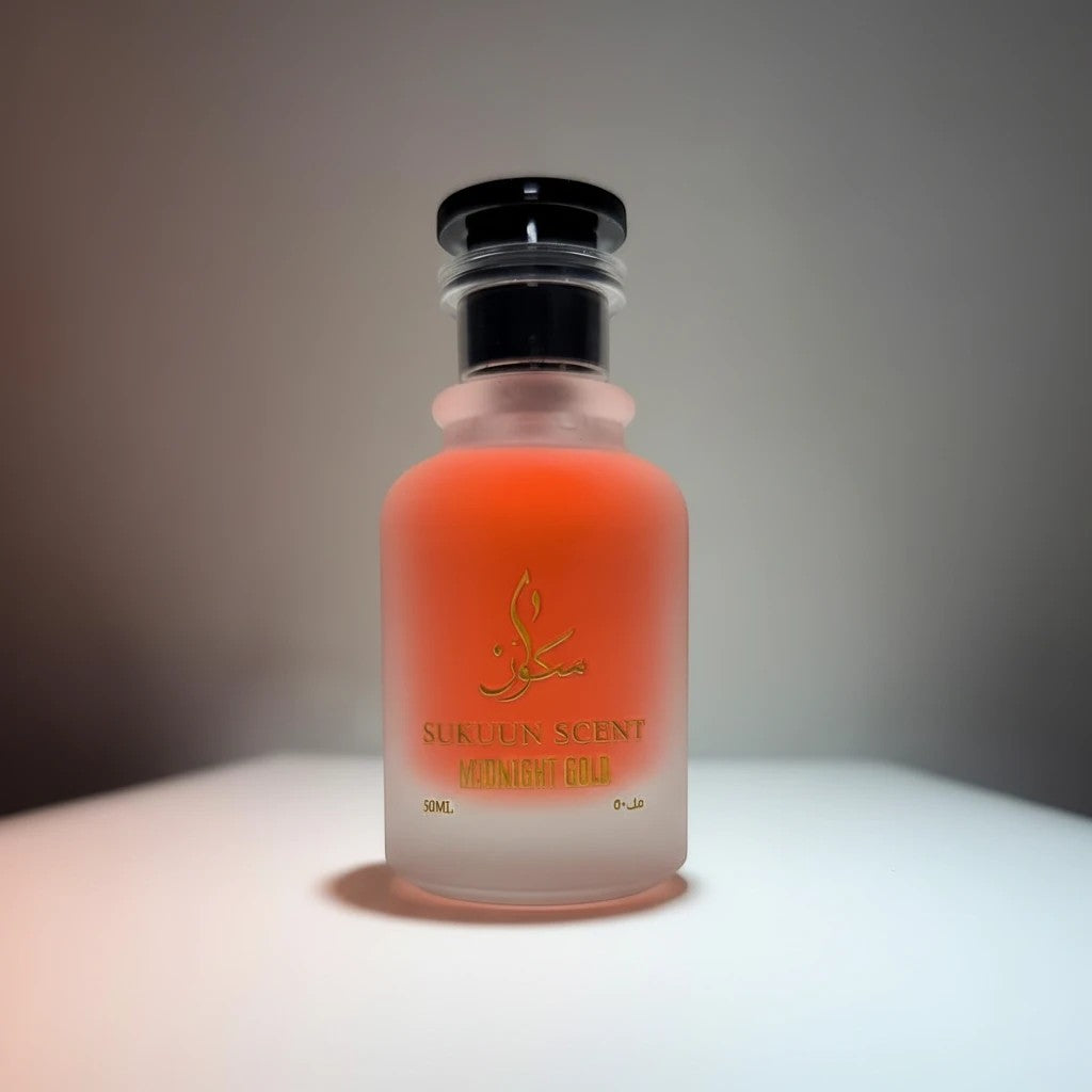 Sukuun Scent Midnight Gold perfume in a frosted glass bottle with orange liquid and gold lettering.
