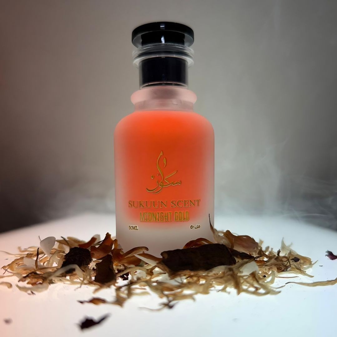 Sukuun Scent Midnight Gold perfume bottle with orange liquid, surrounded by dried botanicals and wisps of smoke.
