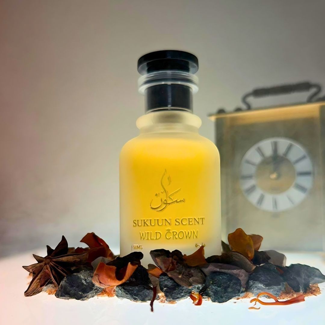 Sukuun Scent Wild Crown Eau De Parfum in a frosted glass bottle, surrounded by spices and stones. Gold text on bottle.